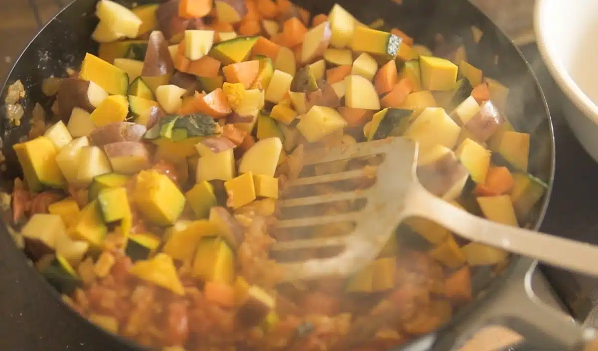 フライパンで玉ねぎ、プチトマト、にんじんなどを炒めている