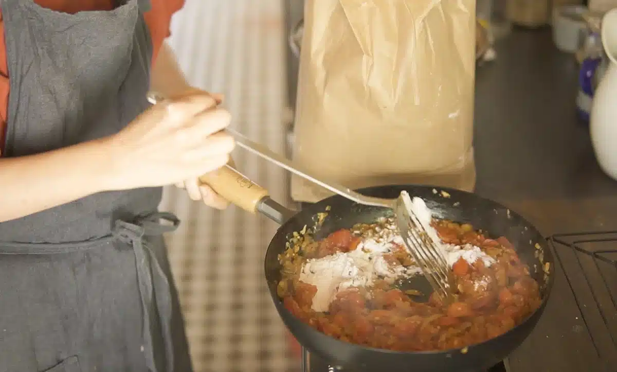 フライパンで玉ねぎ、プチトマト、にんじんなどを炒めている